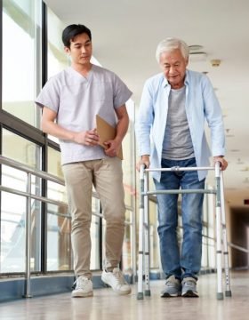 young asian physical therapist working with senior man on walking using a walker